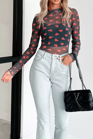 Sheer mesh long sleeve top with red heart print and mock neck, worn with a black cami and light wash jeans.