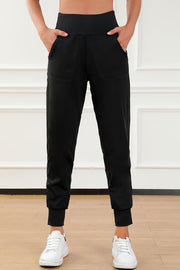 Black joggers with elastic waistband, pockets, and cuffed ankles, styled with white sneakers.