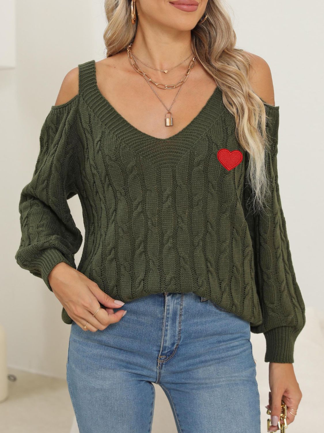 Army green cable knit sweater with open shoulders and a red heart detail.