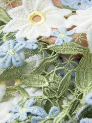 Embroidered floral maxi dress detail with white, blue, and green appliqués and brocade texture.