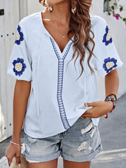 White embroidered yoke sleeve blouse with blue floral details and V-neck tie.
