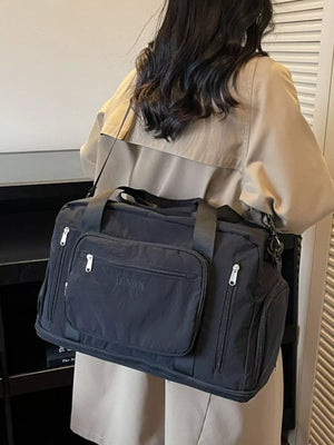 Black canvas duffel bag with multiple zippered pockets and embroidered logo detail.