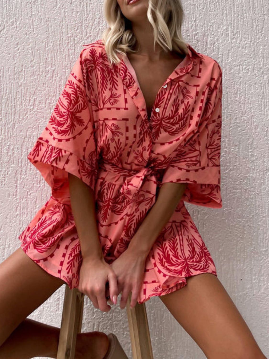 Coral wrap romper with red palm tree print, short sleeves, and tie waist.