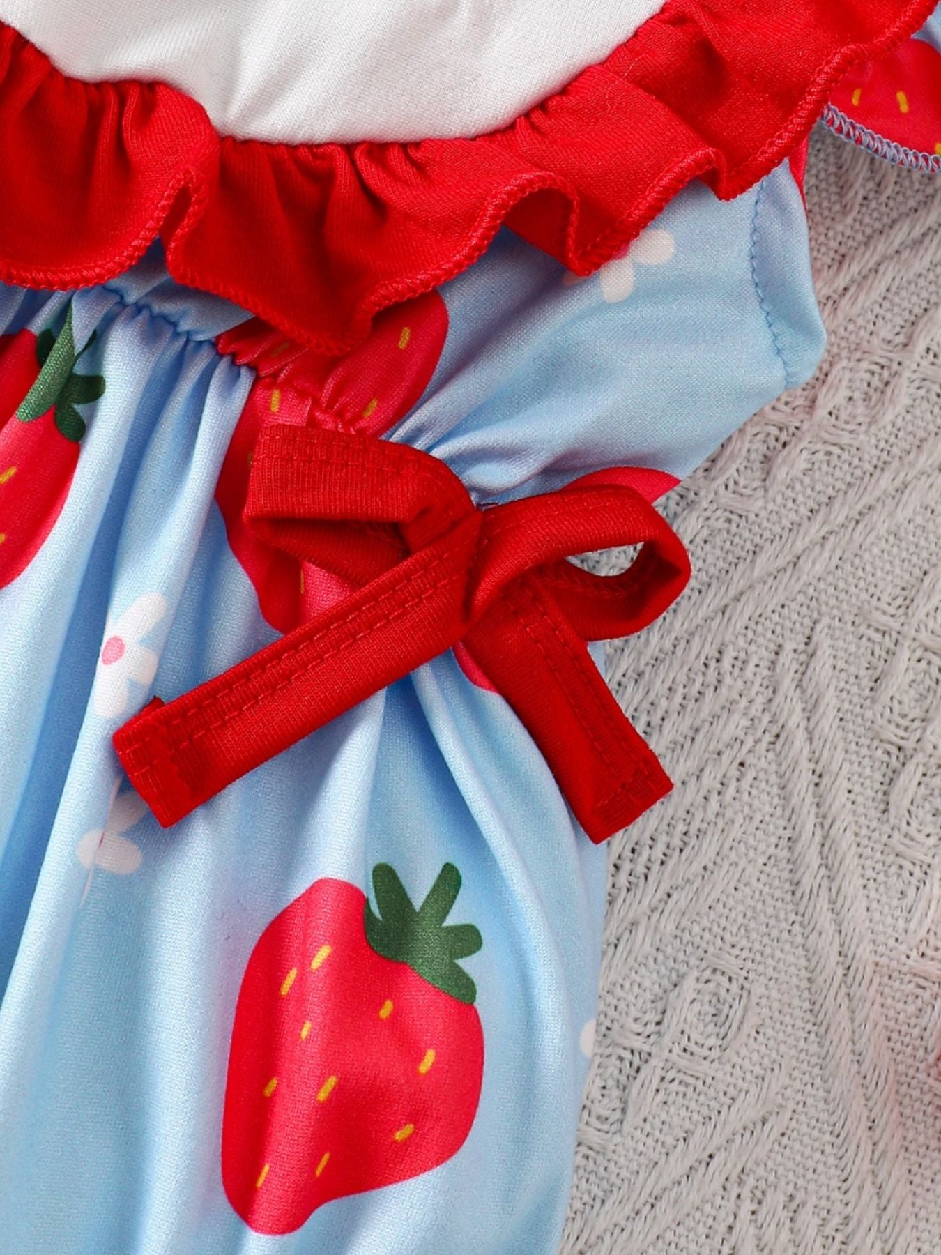 Baby one-piece with strawberry floral print, red ruffles, and bow details.