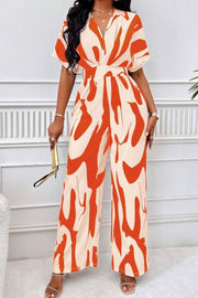 Orange and cream abstract brushstroke wide-leg jumpsuit with short sleeves and a V-neck.