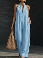 Sky blue halter neck wide-leg jumpsuit with pockets, worn by a model holding a straw bag.