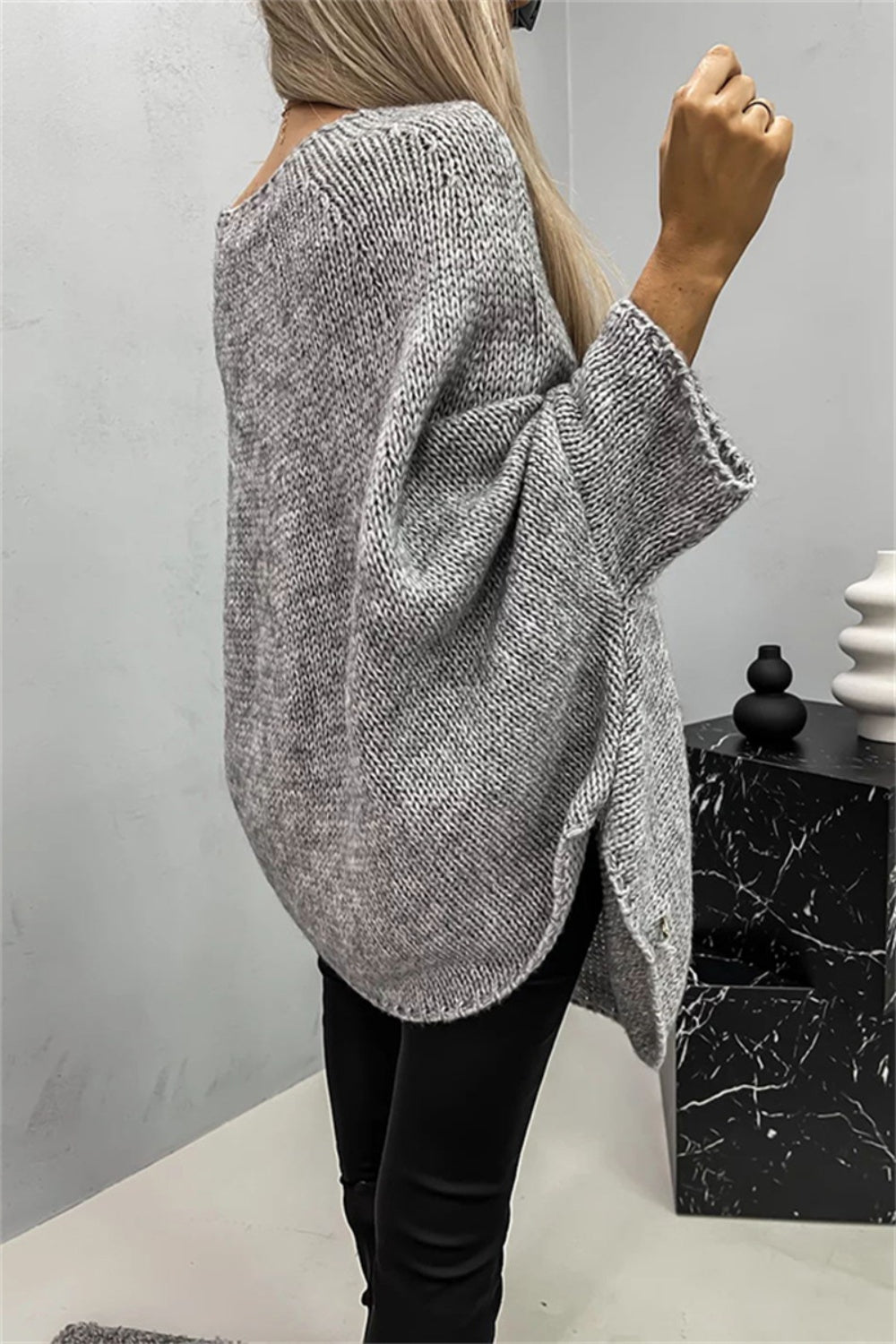 Gray knit sweater with relaxed fit, cape sleeves, and side slits.