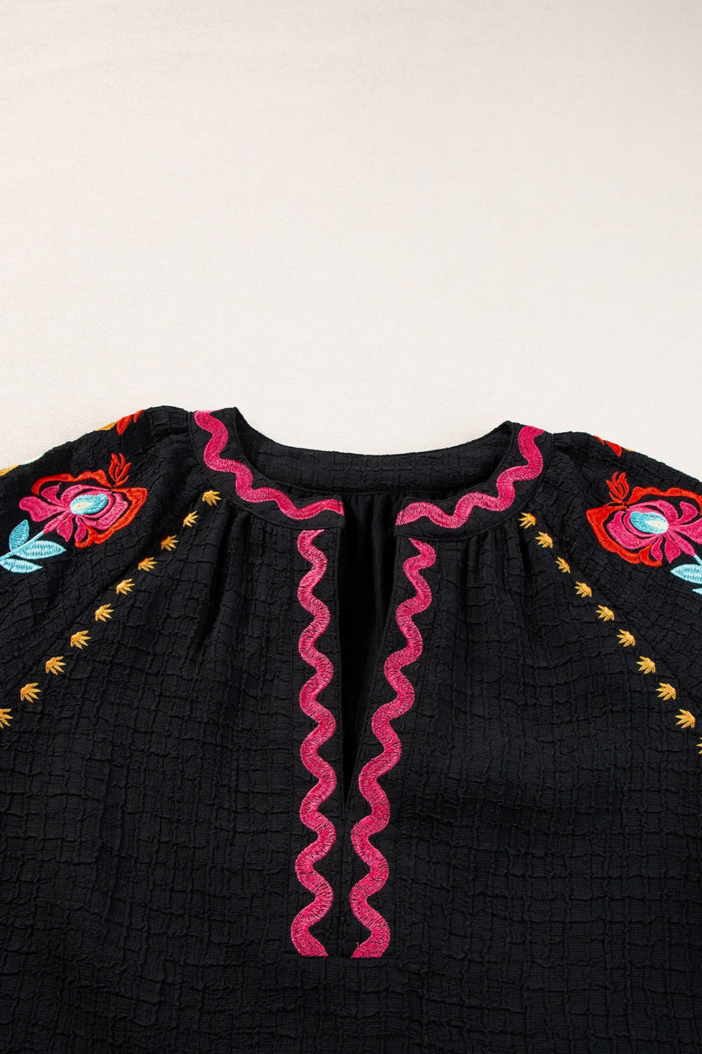 Black embroidered blouse with voluminous sleeves and pink zigzag trim.