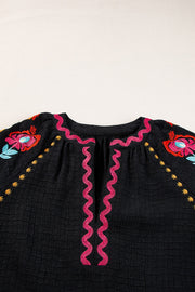 Black embroidered blouse with voluminous sleeves and pink zigzag trim.