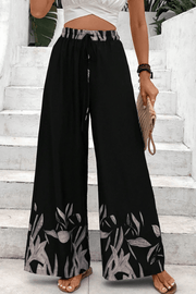 Black wide-leg lounge trousers with botanical print hem and drawstring waist.