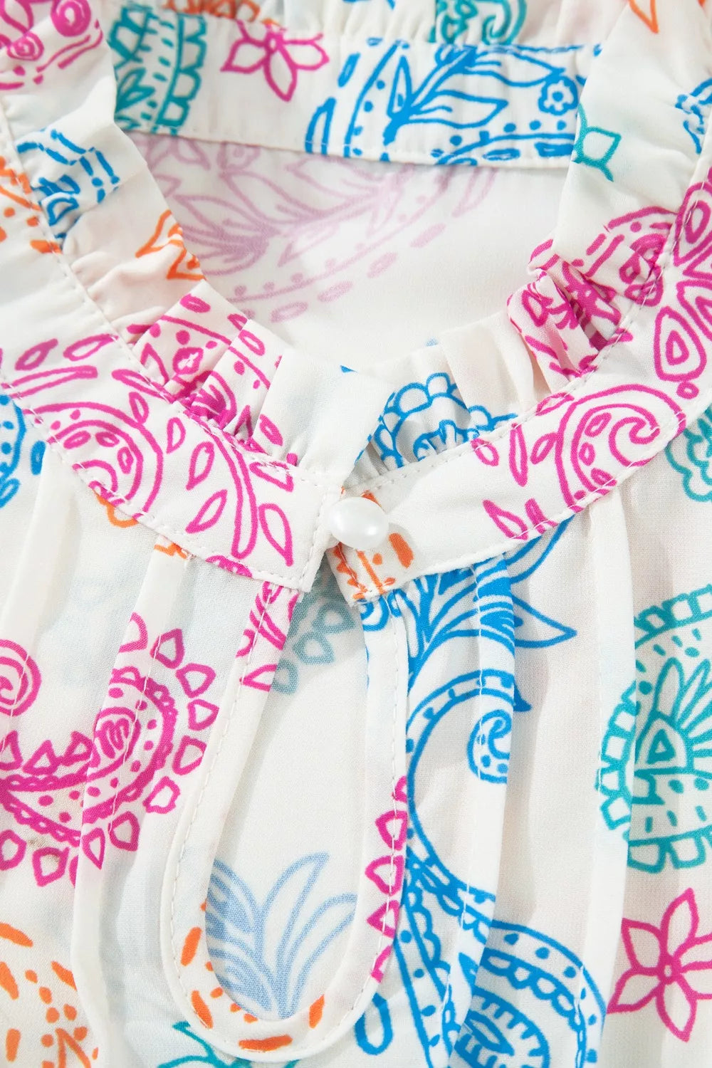 White maternity blouse with vibrant paisley print, ruffled neckline, and button detail.