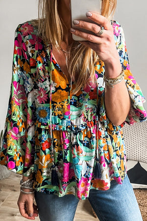 Vibrant floral print peasant blouse with tassel trim and tie neck.