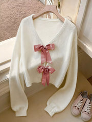 White acrylic knit V-neck cardigan with two pink bow embellishments and balloon sleeves.