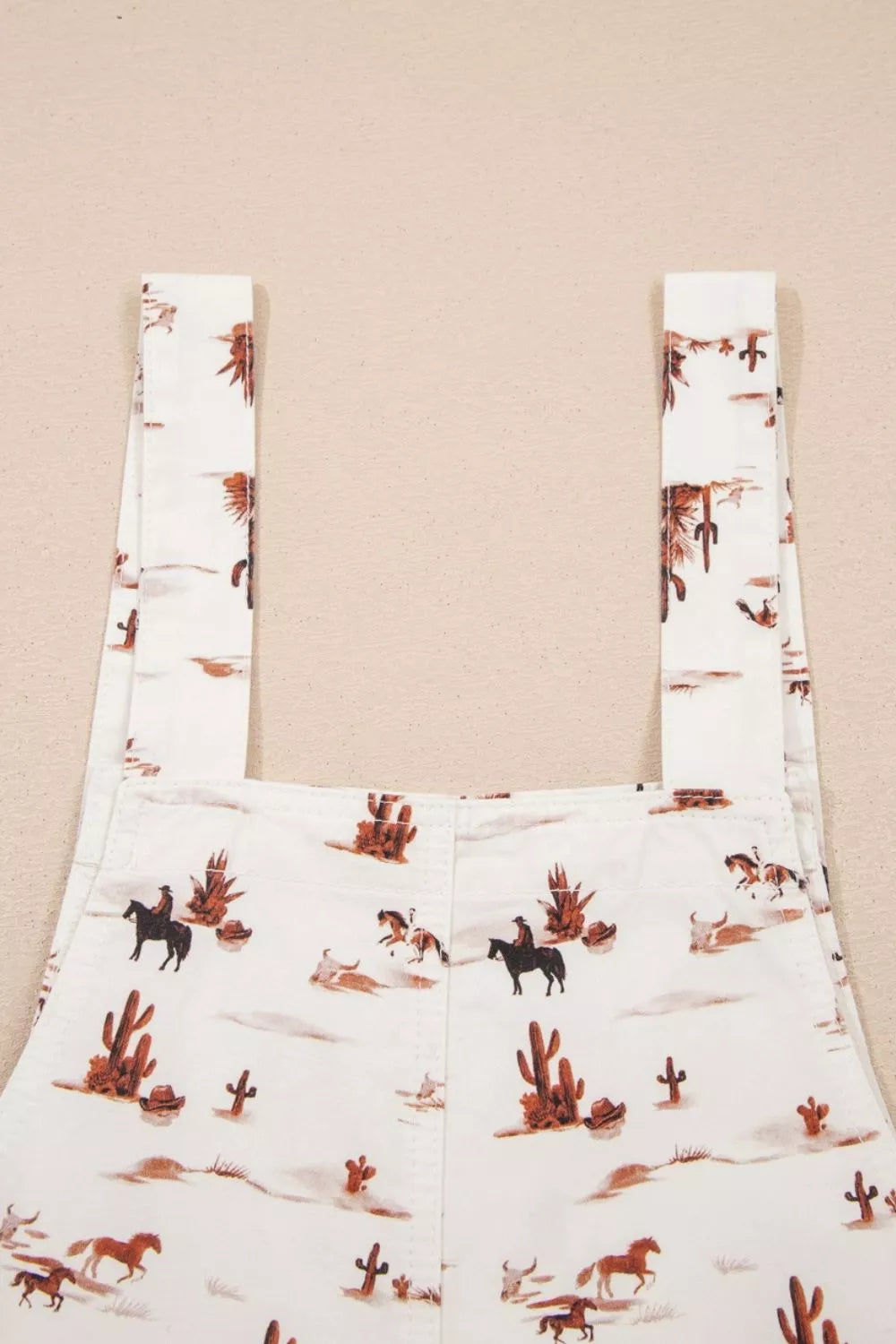 White cotton jumpsuit with desert motif, cowboys, horses, and cacti pattern.