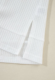 White waffle knit polo shirt with side slits and cuffed sleeves.