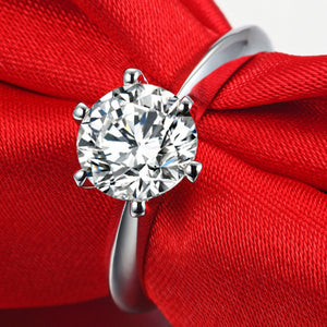 Sterling silver ring with a brilliant cut moissanite solitaire, set on red satin.