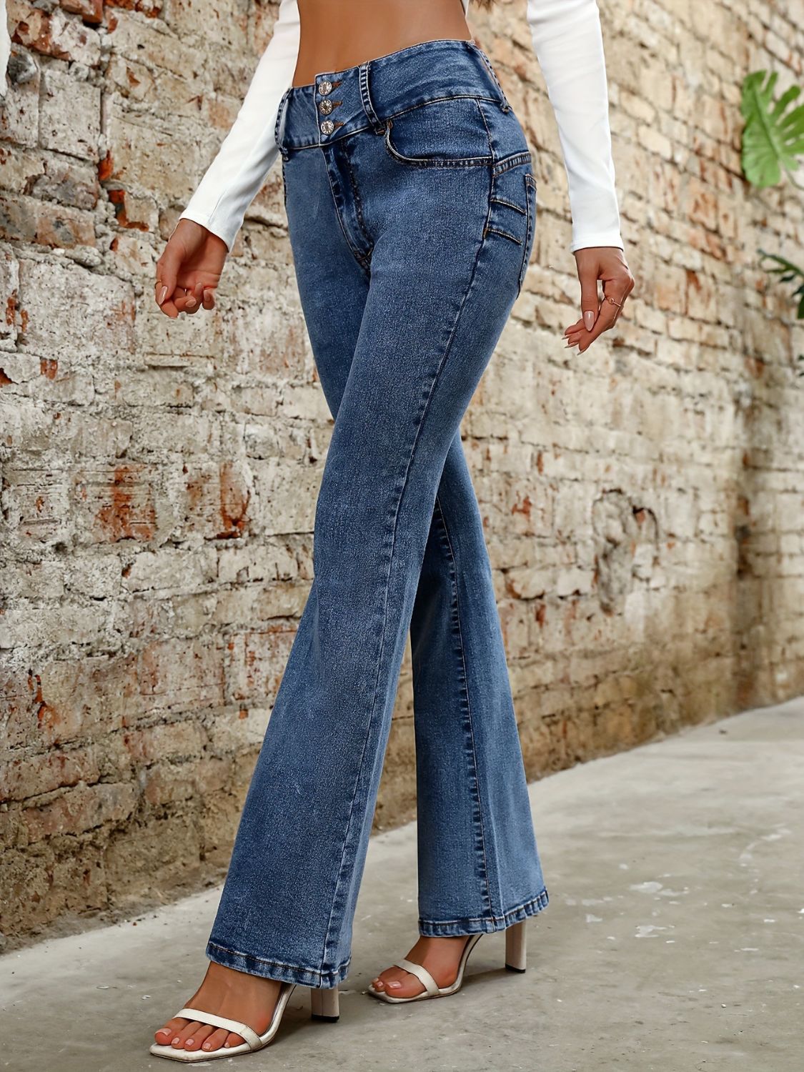 Medium wash denim bootcut jeans with a high rise and button fly, styled with white heels.