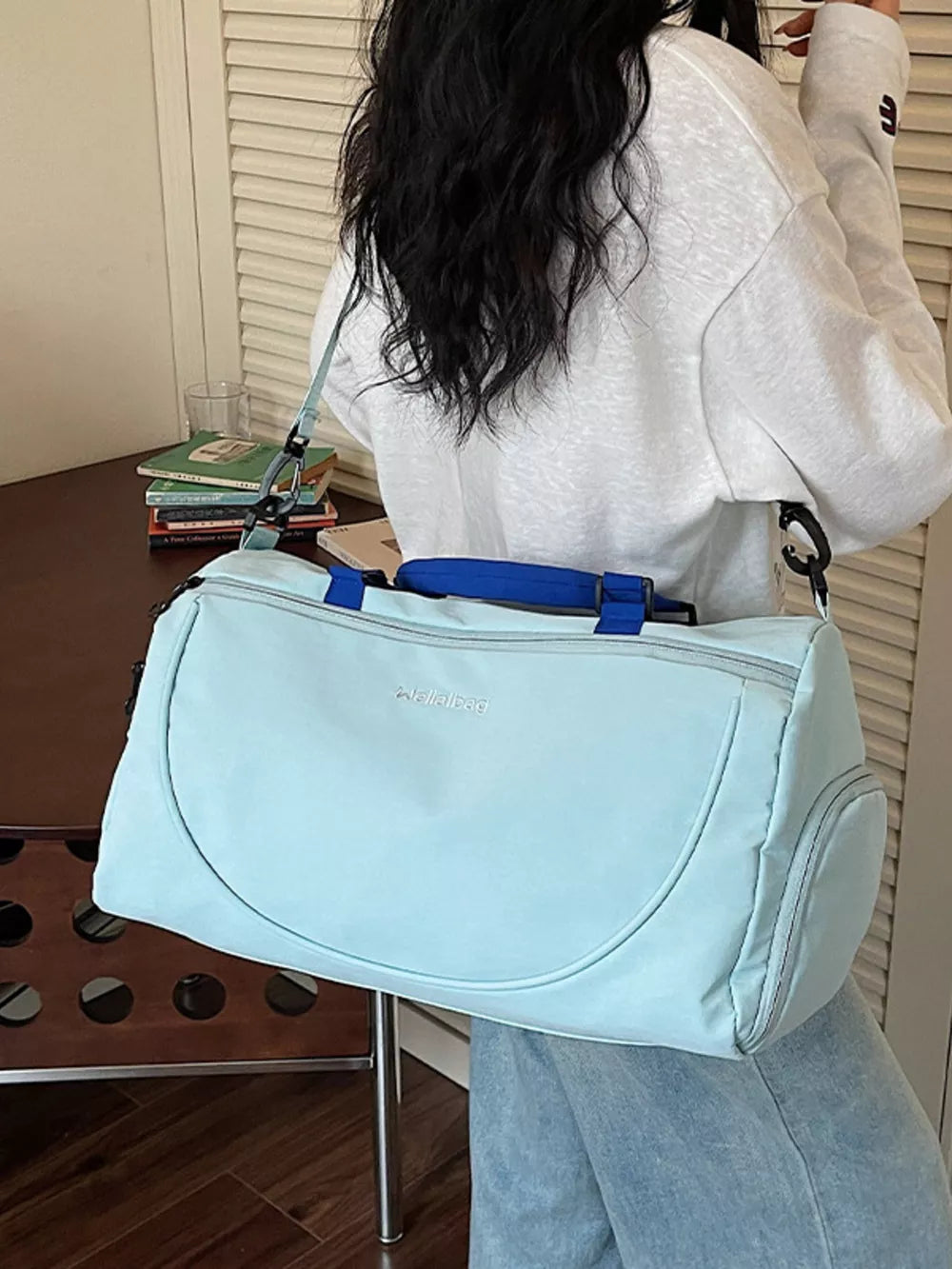 Light blue duffle bag with adjustable strap and blue handles, ideal for gym or travel.