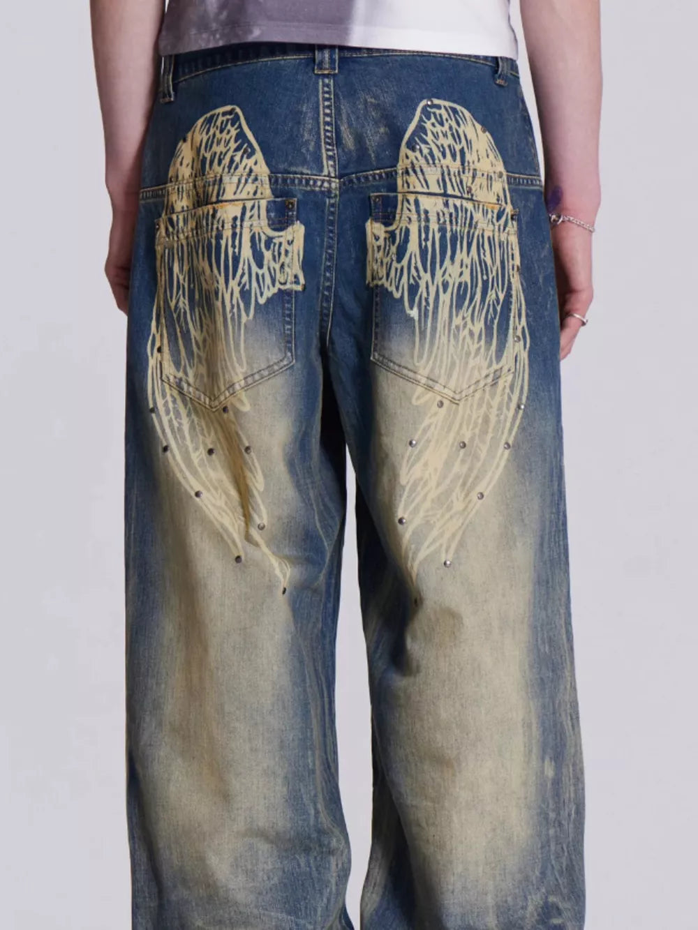 Blue wide leg jeans with vintage wash, studded details, and graphic wing print on back pockets.