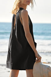 Black linen romper with pockets and a relaxed fit, shown on a model at the beach.