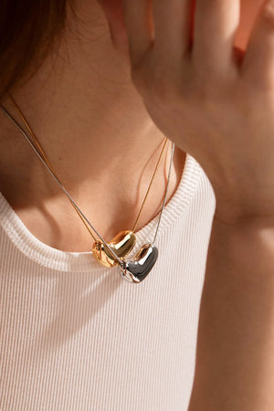 Bean-shaped sculptural pendant necklaces in gold and silver hang on delicate chains.