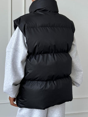 Black padded puffer vest with a high collar, worn over a grey sweatshirt.
