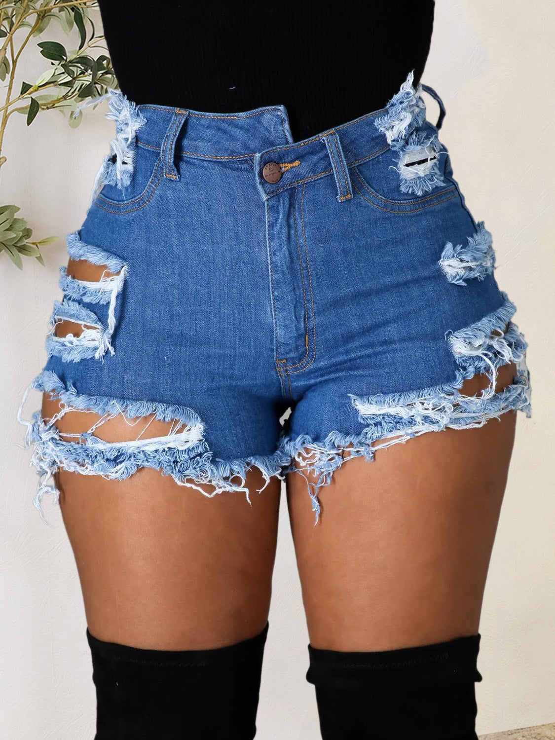 Distressed denim shorts in medium wash with bold cutouts and frayed hem.
