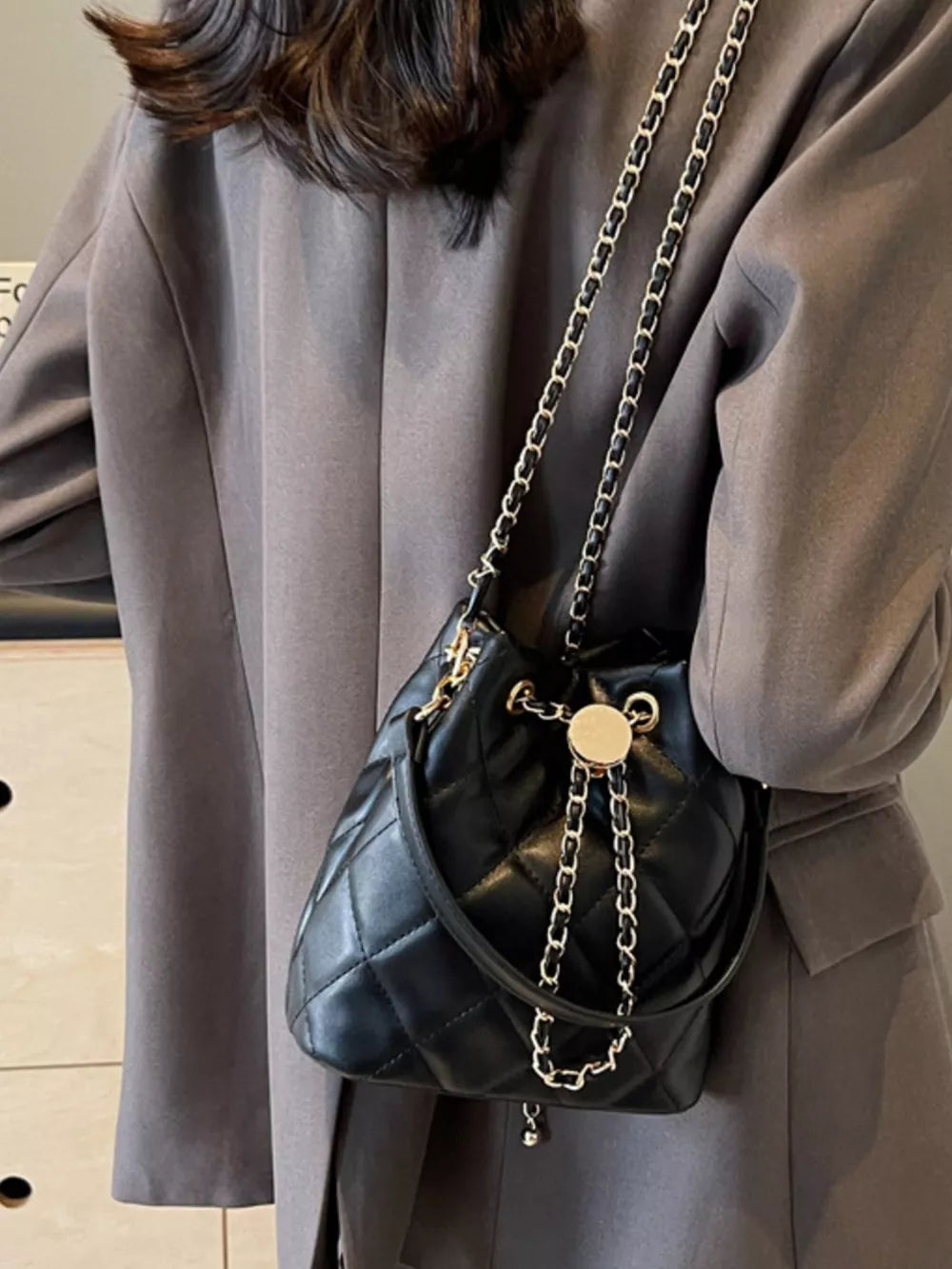 Chic quilted bucket crossbody bag in black with gold chain strap and drawstring closure.