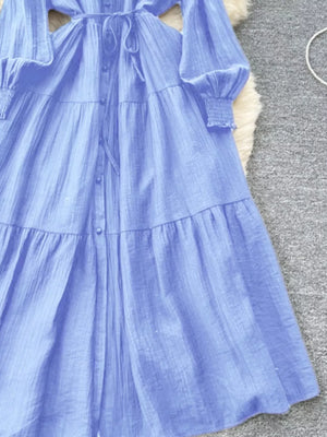 Blue textured tiered long sleeve midi dress with button-down front and tie waist.