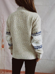 Geometric knit mockneck pullover in neutral tones with blue patterned sleeves.