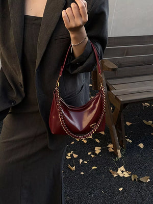 Chic crescent shoulder bag in red with gold chain detail.