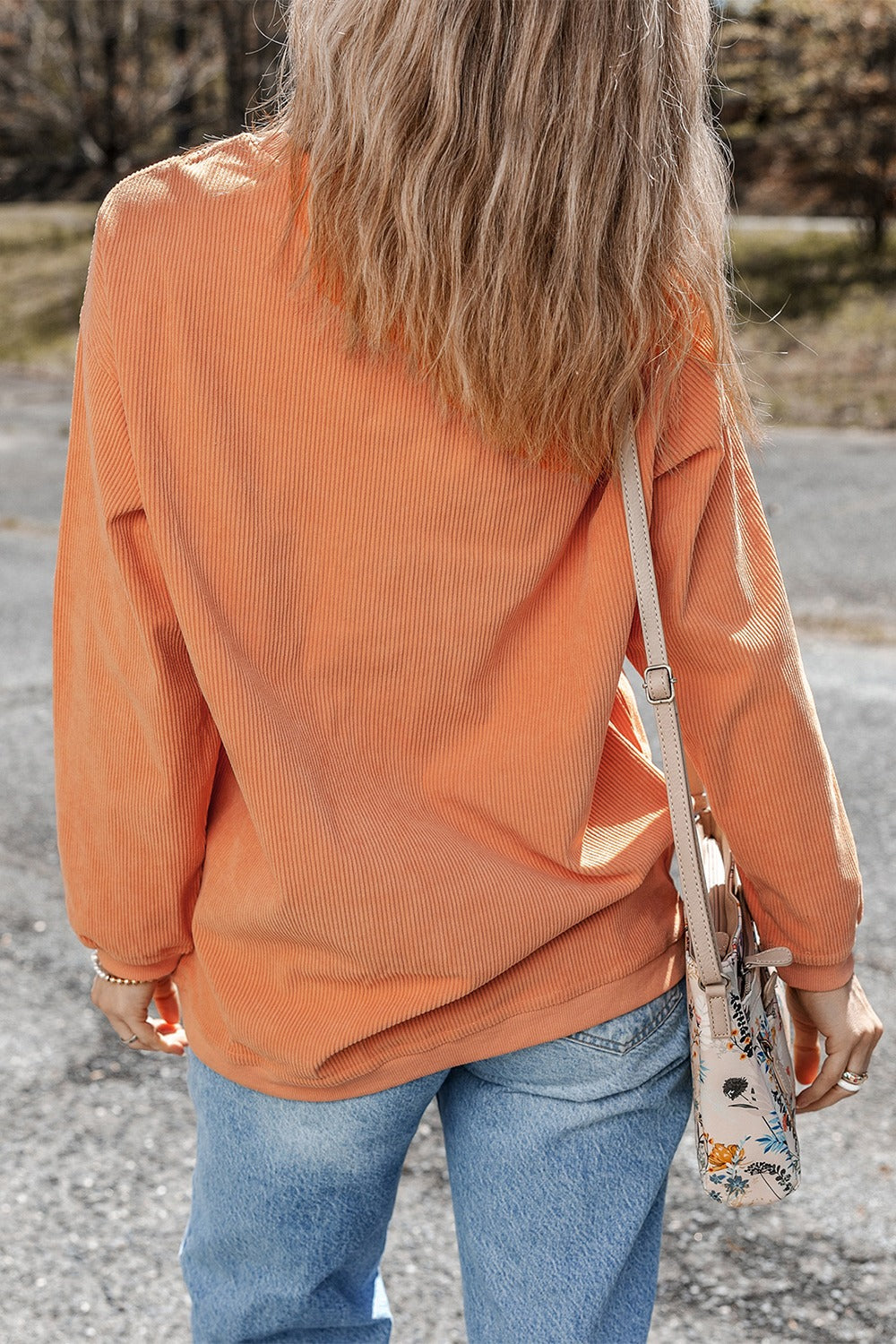 Orange corduroy relaxed sweatshirt with long sleeves, styled with jeans and a floral bag.