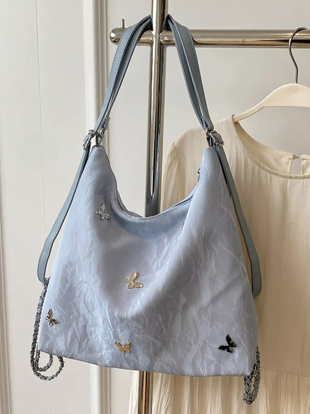 Light blue shoulder bag with butterfly embellishments and chain strap detail.