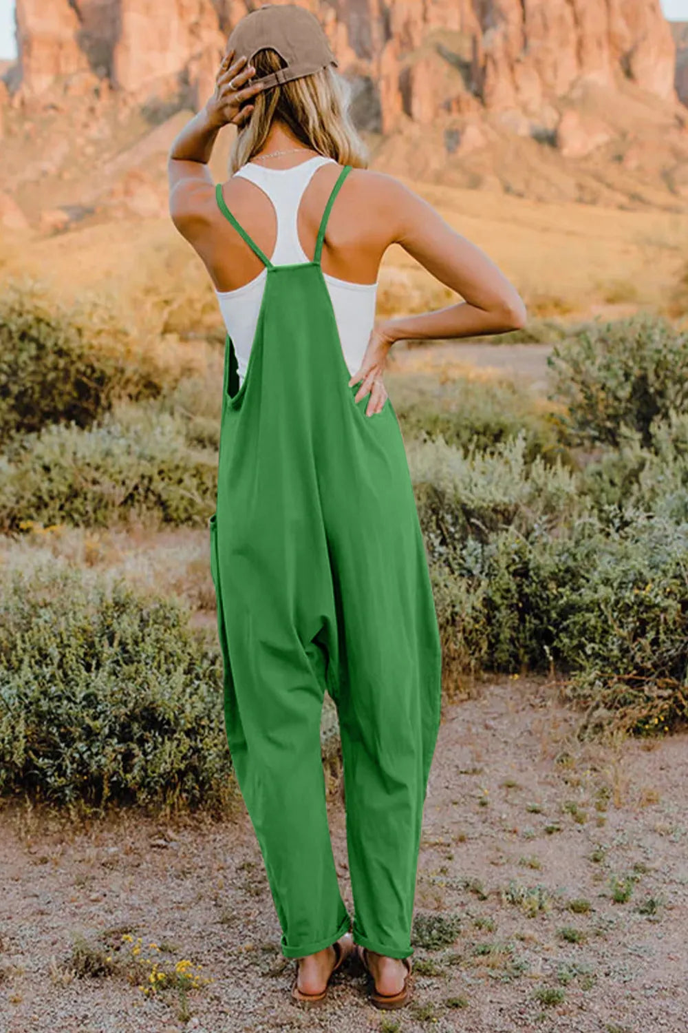Green cotton wide-leg jumpsuit with pockets and V-neck straps, worn with a white tank top.