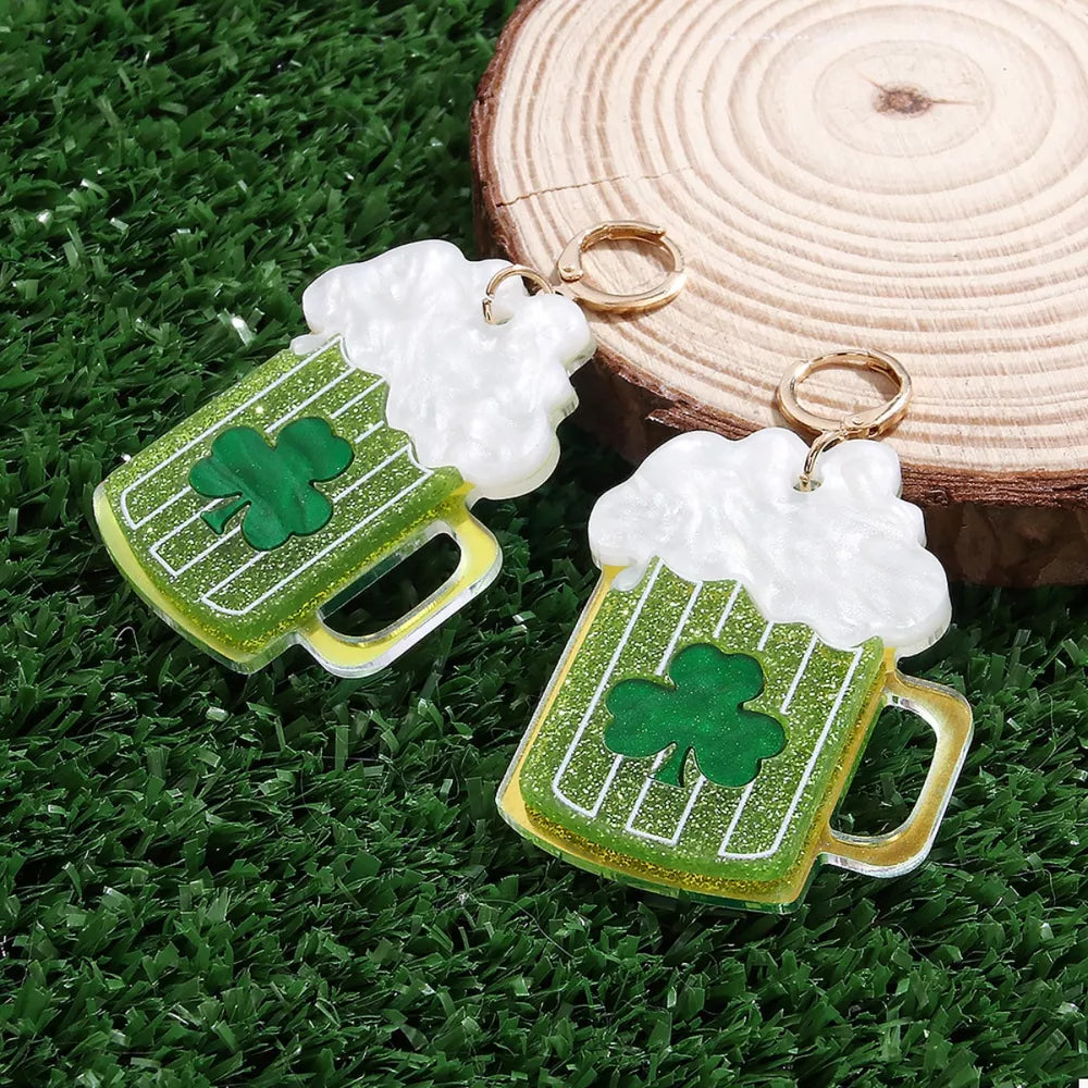 Gold dangle earrings with green beer mug shape, white foam top, and clover detail.
