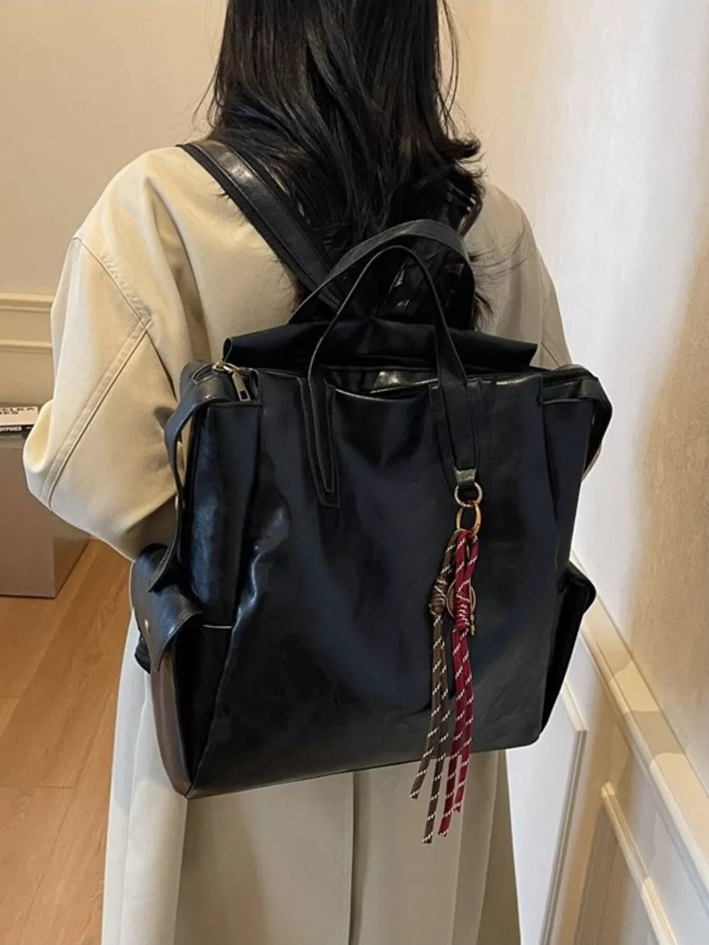 Black leather convertible backpack with tassel charm and side pockets