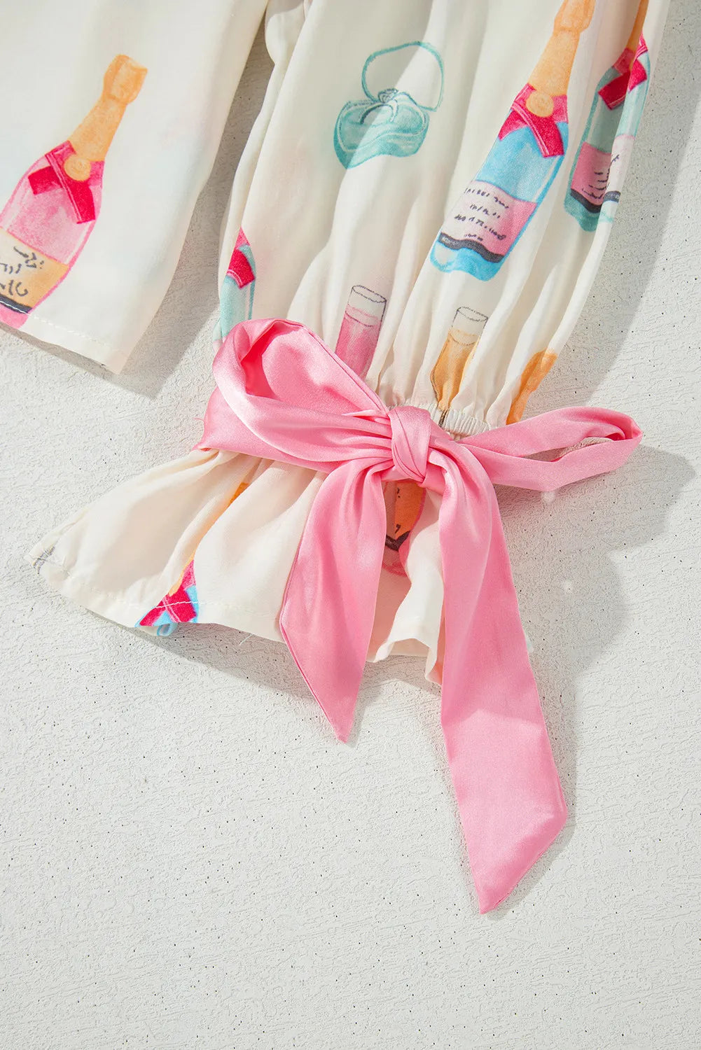 White silk pajama set with champagne print and pink satin bow detail.