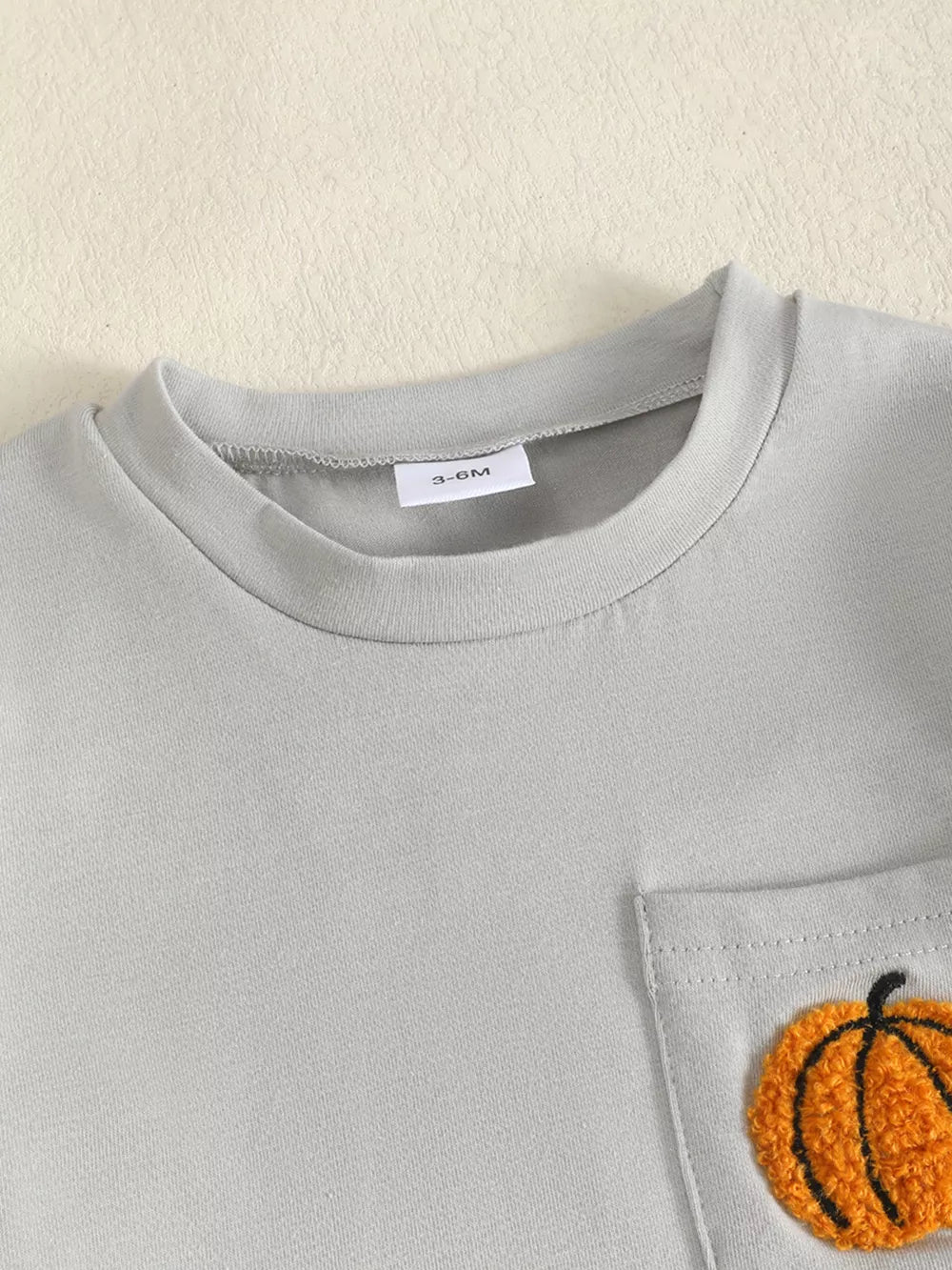 Baby grey t-shirt with orange pumpkin appliqué on chest pocket.