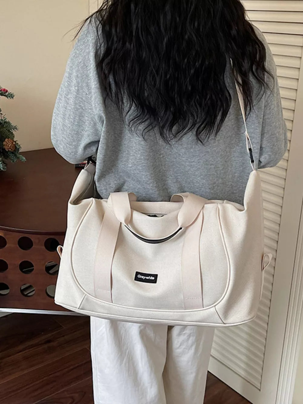Off-white nylon travel duffle bag with curved stitching and adjustable strap.