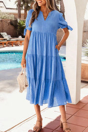 Blue tiered midi dress with notched neckline, short puff sleeves, and tie details.