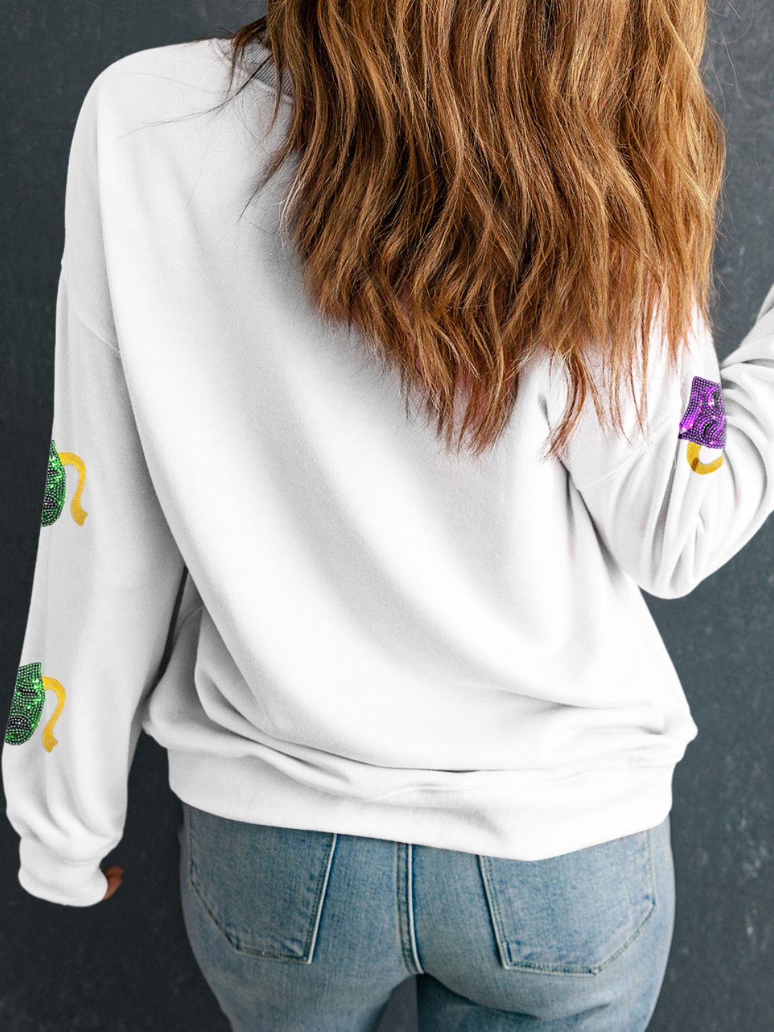 White sweatshirt with sequin mask motifs on sleeves.