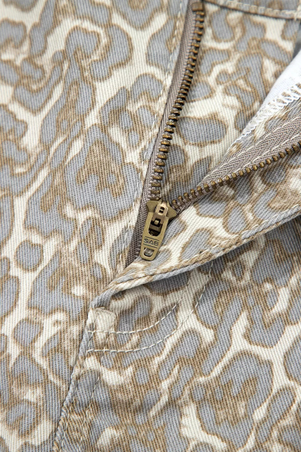 Denim shorts with a grey and beige leopard print and a brass zipper detail.