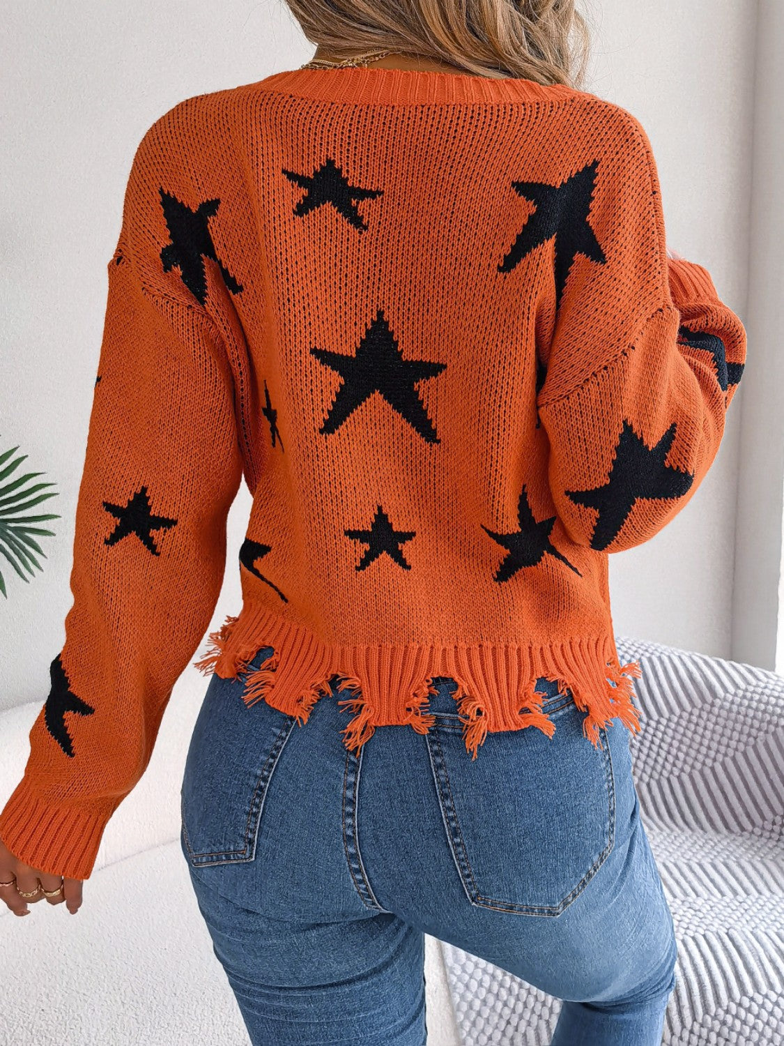 Orange distressed v-neck knit sweater with black star pattern and frayed hem.