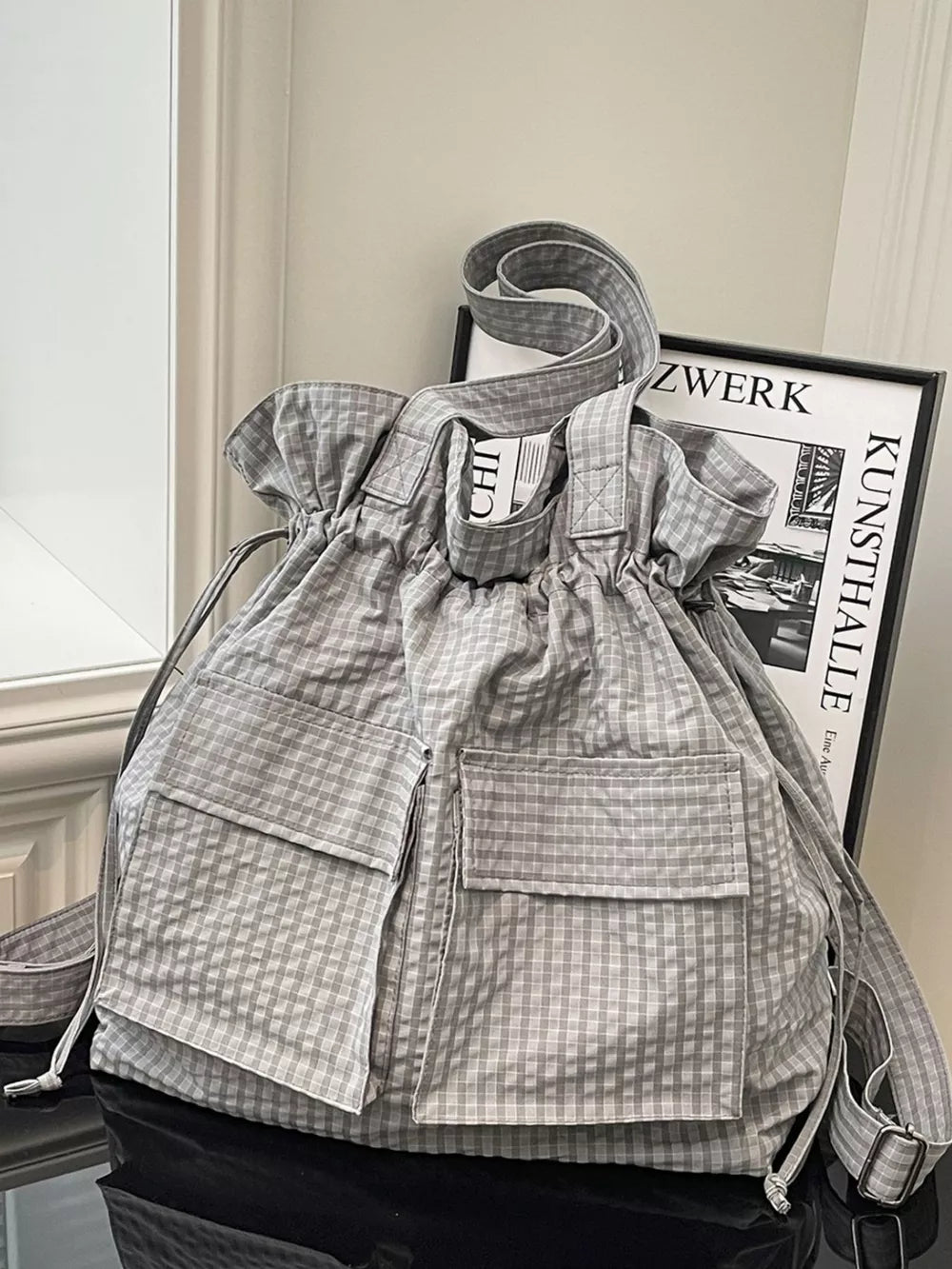 Grey plaid drawstring backpack with front pockets and adjustable straps.