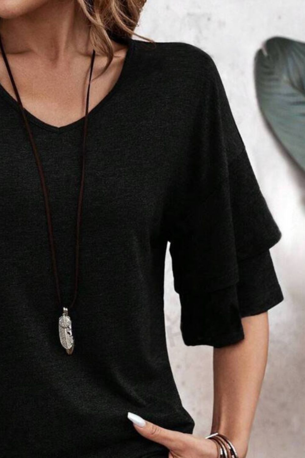 Black jersey tee with tiered short sleeves and V-neck, styled with a feather pendant necklace.