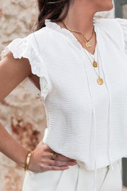 White textured tie-neck blouse with eyelet trim flutter sleeves and ruffled neckline.