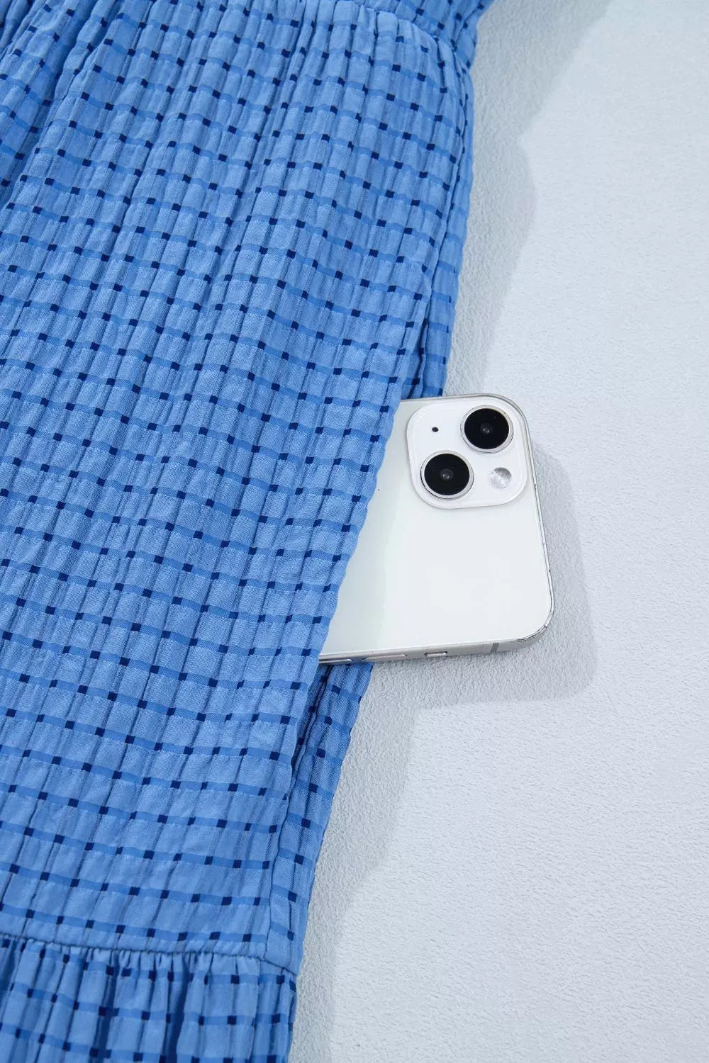 Blue tiered midi dress with a subtle checkered pattern and a phone in the pocket.