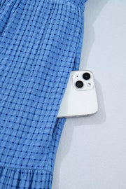Blue tiered midi dress with a subtle checkered pattern and a phone in the pocket.