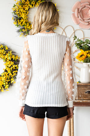 White knit blouse with sheer floral appliqué sleeves and textured front.