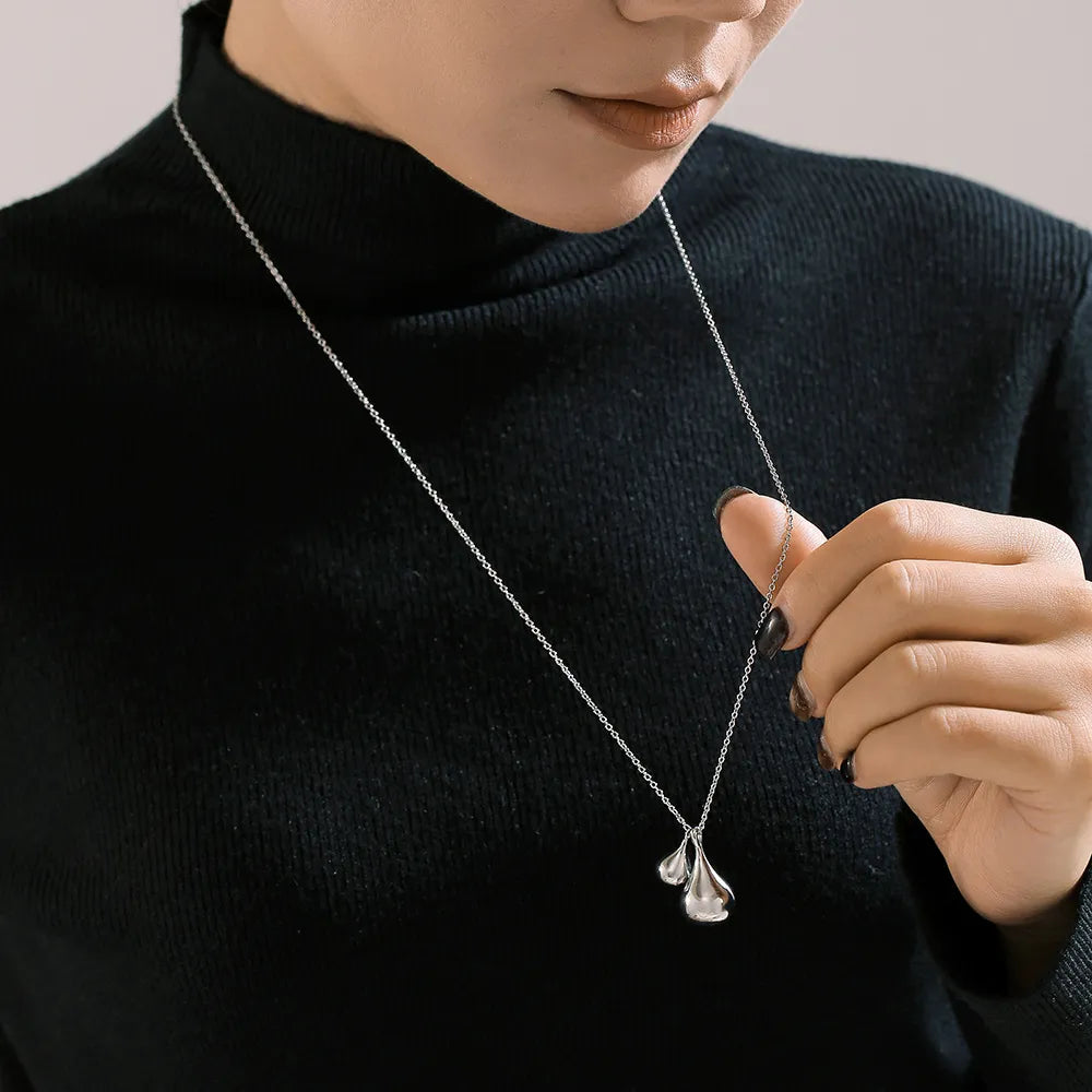 Silver sculptural duo pendant necklace with a delicate chain, styled on a model.